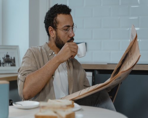 Man drinking coffee and reading morning news in a sunny kitchen